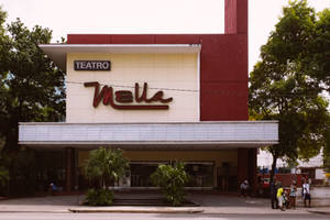 Teatro Mella劇院建築，外面有棕櫚樹和行人。
