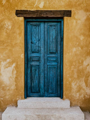 一扇質樸的藍色木門，由帶紋理的赭色牆壁和石階框住。