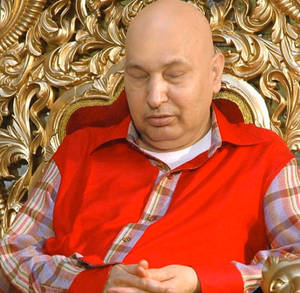 一個光頭男人穿著紅色背心在華麗的金色王座上睡覺。
