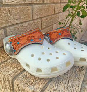 白色Crocs鞋，帶有裝飾性皮帶和綠松石，放在石面上。