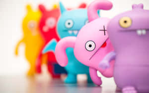 一排色彩繽紛的Uglydoll玩具，其中一個粉紅色公仔處於焦點。 — 怪獸動圖 壁紙