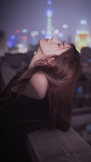女性在屋頂上休息，身後的城市燈光在夜晚閃爍。