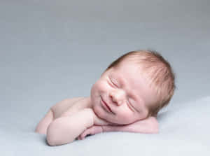 一個睡著的新生嬰兒，帶著溫柔的微笑，躺在灰色毯子上休息。