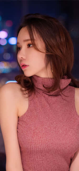 身穿粉紅色上衣的女性若有所思地看著夜晚的城市燈光