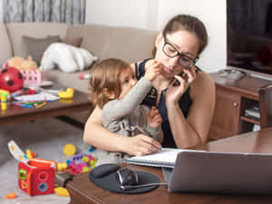 一位母親在雜亂的客廳中抱著幼兒，同時在筆記型電腦和手機上工作。