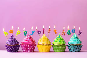 五個杯子蛋糕，上面有燃燒的字母蠟燭，拼出 happy birthday。