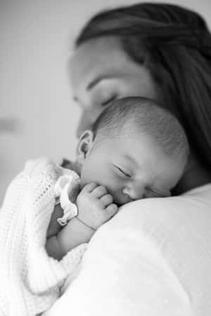 母親輕輕抱著包裹在針織毯中安睡的新生嬰兒。