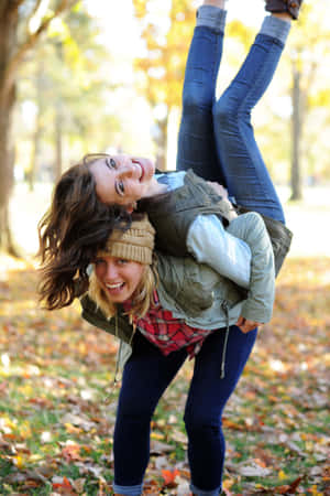 兩位女士喺樹葉茂密嘅秋日公園入面，邊笑邊玩味十足咁翻轉。
