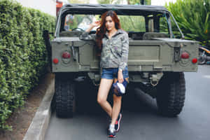 身穿迷彩外套和牛仔短褲的女子在綠色軍用吉普車旁擺姿勢。