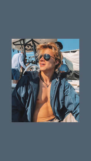 戴太陽眼鏡和藍色外套的年輕男子在夏日陽光下於船上微笑。