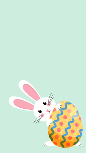 一隻卡通兔在薄荷綠色背景上抱著一個裝飾過的復活節彩蛋。 — 可愛兔仔 壁紙