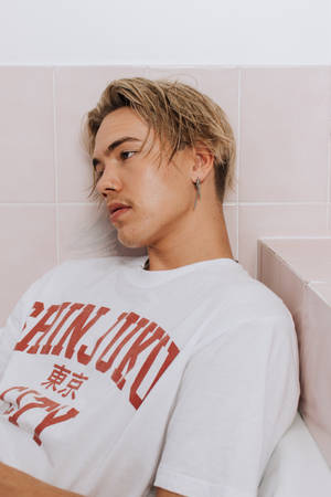 身穿白色T恤的年輕男子靠在粉紅色瓷磚牆上。
