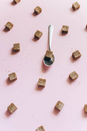 銀匙揸住一粒糖方塊，周圍散落住糖方塊喺粉紅色背景上。