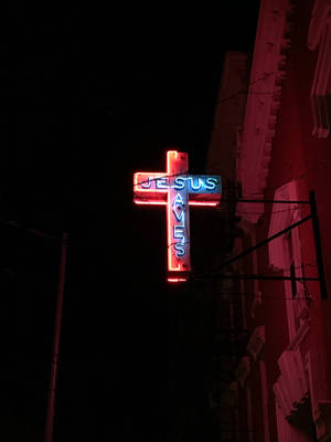 寫著「Jesus Saves」的霓虹十字架在夜晚的城市街道上發光。 — 耶穌基督 壁紙