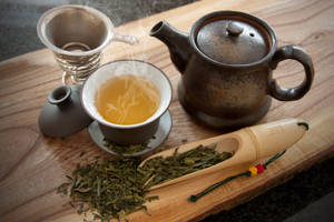 一杯冒煙的綠茶配茶壺和竹茶匙在木桌上。