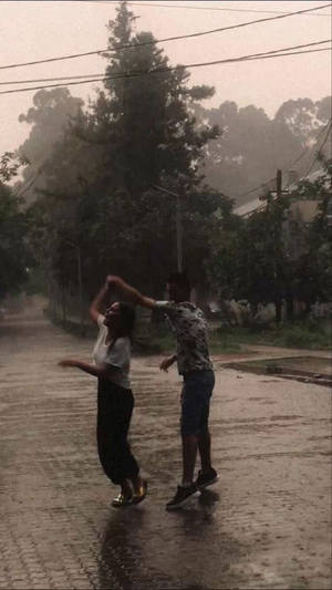 兩個人在雨中，在濕漉漉的街道上跳舞，背景有樹木。
