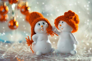兩個戴著橙色針織帽的雪人公仔，在雪地節日場景中，周圍有閃爍的裝飾。