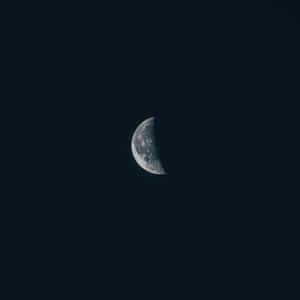 一彎月牙掛在黑暗的夜空中，可見隕石坑。