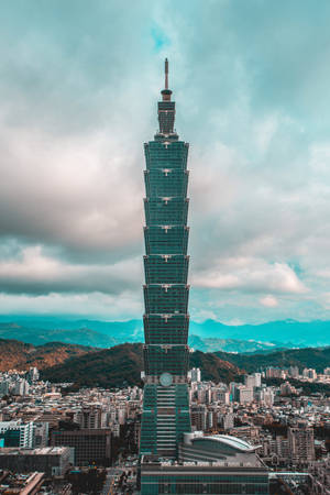 台北101摩天大樓聳立在密集的城市之上，背景有山脈。
