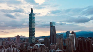台北101大樓在日落時分，背後襯著山巒，聳立在密集的城市之上。 — 唐人街 GIF 壁紙
