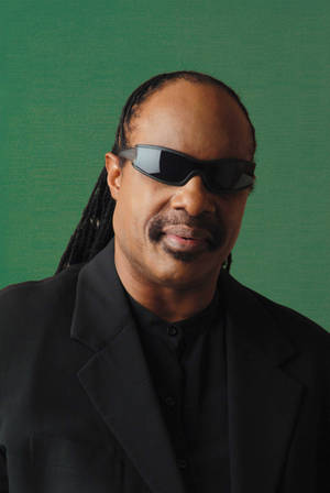 Stevie Wonder戴上太陽眼鏡和黑色西裝，在綠色背景前。