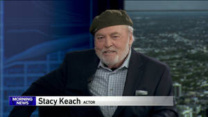 演員 Stacy Keach 在工作室接受訪問，身後是城市景色。
