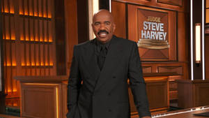 Steve Harvey 在電視節目場景中穿著黑色西裝微笑。 — 黑色動態圖 壁紙