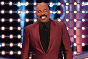 Steve Harvey 身穿栗色西裝，在明亮的舞台上微笑。
