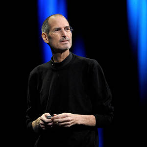 Steve Jobs 在藍色燈光的舞台上手持裝置。