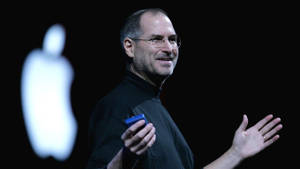Steve Jobs 在舞台上進行演示，身後有發光的 Apple 標誌。