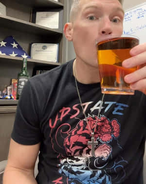 男子穿著圖案T恤和十字架項鍊在室內飲用琥珀色飲料