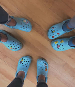 四個人穿著貼有卡通貼紙的淺藍色Crocs鞋站在木地板上。