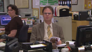 Dwight Schrute 在 Dunder Mifflin 辦公室拿著雜誌，眼神專注。