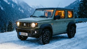 綠色鈴木 Jimny 在夜間積雪的山路上行駛，車內有溫暖的燈光。