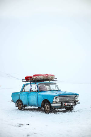 復古藍色汽車，車頂有皮划艇，停在雪地