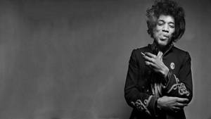 Jimi Hendrix 身穿黑色外套，手持香煙，表情頑皮。