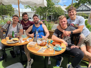 五個男人在陽光明媚的日子裡在戶外咖啡館一起享用美食。