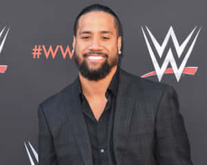 WWE摔角手在記者會上身穿深色格紋西裝對著鏡頭微笑。