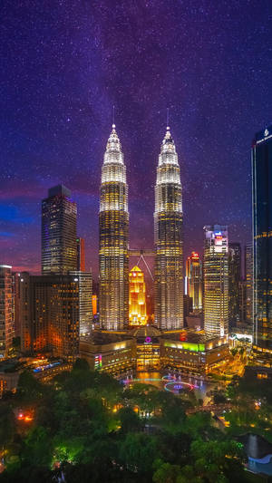 Twin towers illuminated at night under a starry sky with city lights and greenery below. — 香港 壁紙