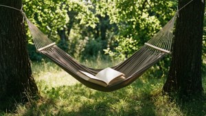 樹間的吊床在陽光普照的森林空地中托著一本打開的書。