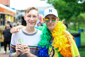 兩名快樂的男子在Pride慶祝活動中，臉上塗著彩虹顏料，戴著羽毛圍巾。