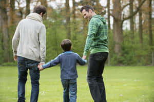 兩個男人和一個孩子喺有秋天樹嘅公園入面手拖手。
