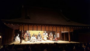 身穿傳統服飾和面具的能劇演員在夜間木製舞台上。
