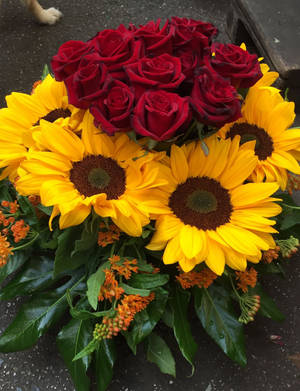紅玫瑰、黃向日葵、橙色花朵和綠葉的花束。