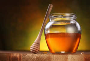 金黃色蜂蜜玻璃罐和木製蘸料棒在木質表面上。