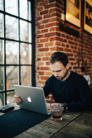 男人在磚牆咖啡館的木桌上使用手提電腦工作，有咖啡。