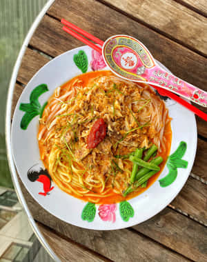 一碗色彩繽紛的湯麵，配上配料，放在木桌上，旁邊有紅色筷子。 — 4:5 壁紙