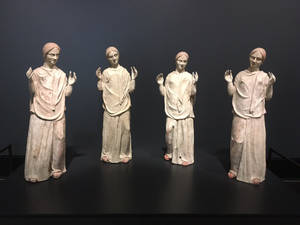 四個身穿長袍、舉起雙手的相同古代雕像在博物館展出。 — 雕塑 壁紙