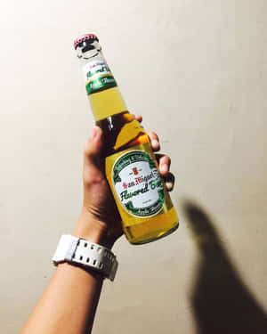 手戴手錶拿著蘋果味啤酒瓶靠牆。 — 4:5 壁紙