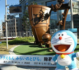 藍色機械人吉祥物在城市公園的銅門雕塑前微笑。